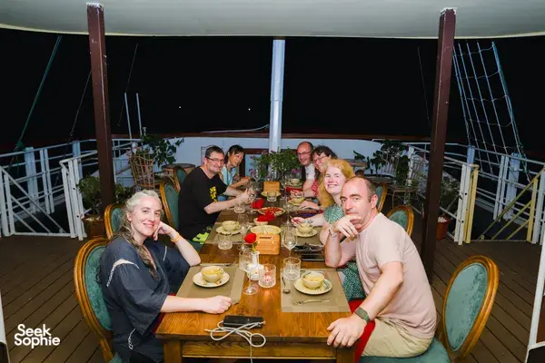 Group dinner on the open-air deck of a Cat Ba cruise boat with shared plates and drinks under evening lights