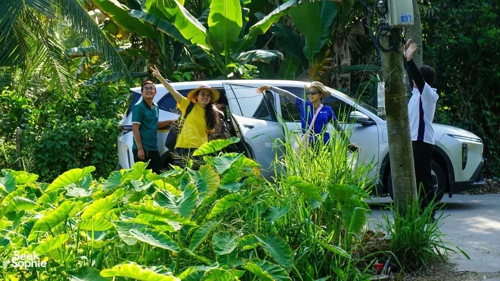Tour riders smiling beside a parked support vehicle surrounded by lush greenery on Mekong Island near Ho Chi Minh City