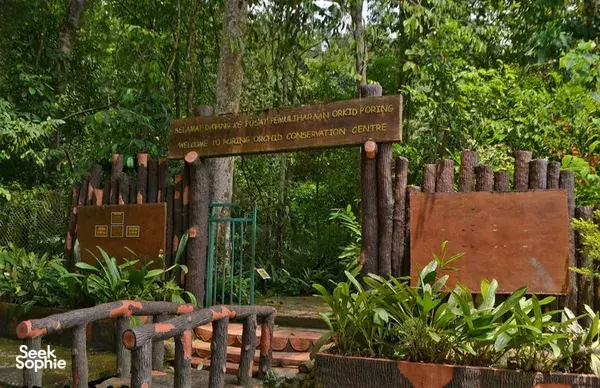 Wooden gate sign reading Welcome to Orchid Conservation Centre surrounded by plants and rustic fence posts in a garden