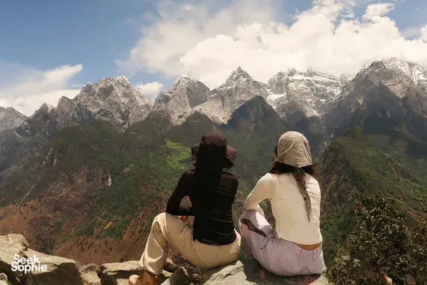 Two travellers sitting on a cliff watching the snow-dusted peaks of Tiger Leaping Gorge, Lijiang, on the 2D1N high trail