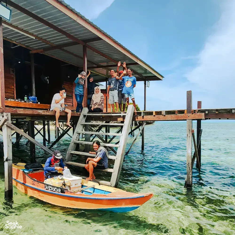 Small group boarding a skiff from a sea-lodge jetty in Semporna, wearing life jackets for a dive-and-stay day