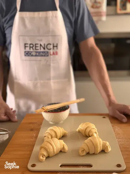 Di bengkel di Singapura, pembuat pastri dari French Cooking Lab menyusun doh croissant di atas papan kayu, dengan dulang dan peralatan berdekatan