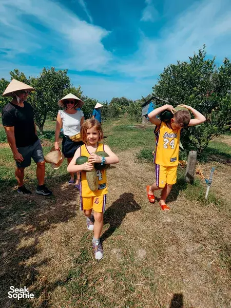Straw-hat children walking along an orchard path with adults at Cam Farmstay Cu Chi, Cu Chi countryside