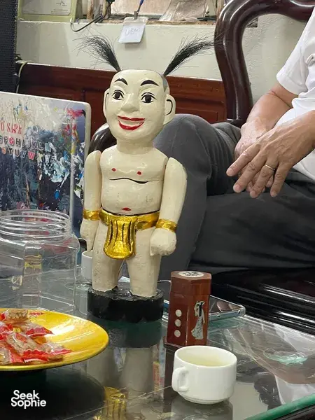 Figur boneka air kayu berlukis di atas meja pajangan dengan cangkir teh dalam pengalaman wayang air privat di Hanoi oleh Bamboo Life