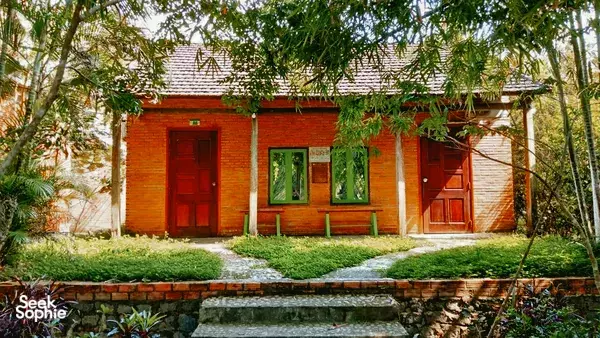 Traditional lodge façade with red doors and garden path at Green Hope Lodge, set among bamboo and shrubs in Cat Tien