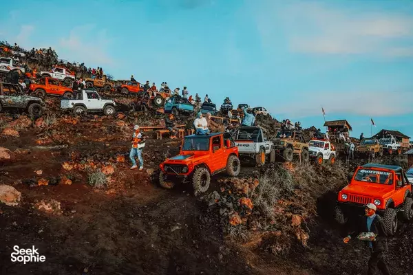 Jeep convoy climbs a rugged hillside at dawn with riders lined along orange and red 4x4s on Mt Batur