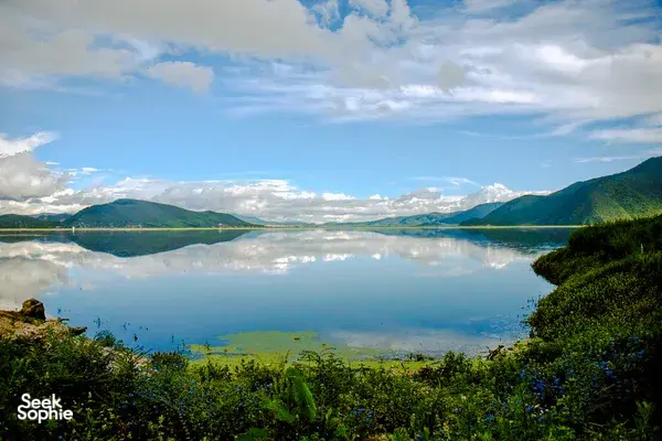 Calm Napa Lake in Shangri-La framed by forested hills and mountains under cloudy skies, with mirror-like reflections