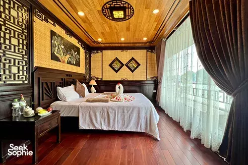 Wood-panelled cabin bedroom on a Cat Ba Ocean Cruises 2D1N Cat Ba cruise, with a dressed bed and floor-to-ceiling curtains by the window