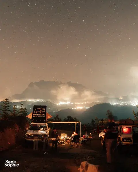 Starry night wild camping with a campfire and vans at a ridge, looking towards Mt Kinabalu from Kota Kinabalu