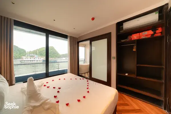 King bed in Cat Ba cruise cabin with floor‑to‑ceiling windows overlooking the bay and limestone hills