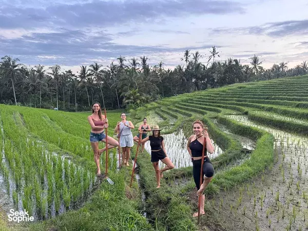 Travellers walking barefoot along Bali rice terraces during a 4D3N Ancient Yoga Retreat, with lush fields stretching into the horizon