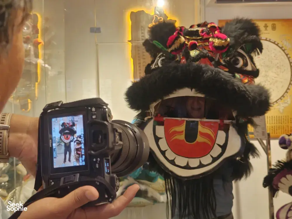 Traditional lion dance performer wearing an ornate headpiece stands while a camera films inside a Ho Chi Minh City cultural heritage room