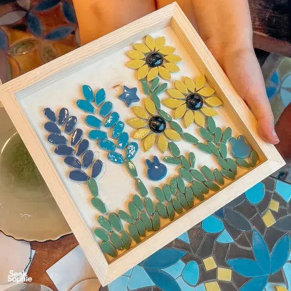 Hand placing small ceramic tiles into a flower mosaic artwork in an artspace for Bat Trang pottery village crafts near Hanoi
