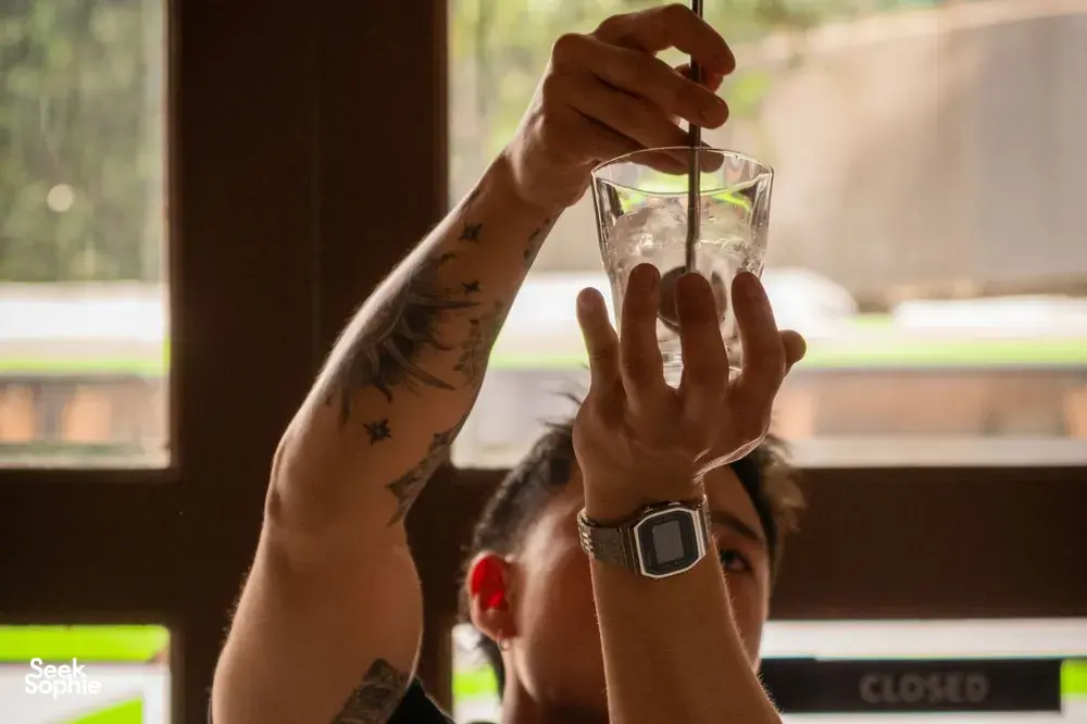 Guests clink cocktail glasses during a craft tasting in an intimate Singapore bar, with warm light and ice-filled pours.