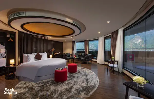 Luxury bedroom on the Oasis Bay Party Cruise with a round ceiling light, bedding and large windows over Halong Bay