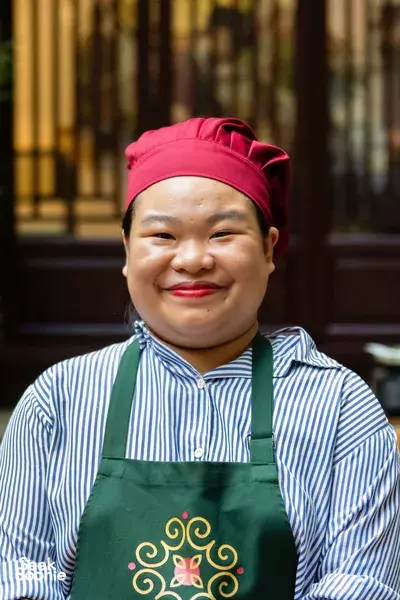 Cherry, the Hanoi culinary host, smiling in her red headscarf and green apron in a cosy home kitchen