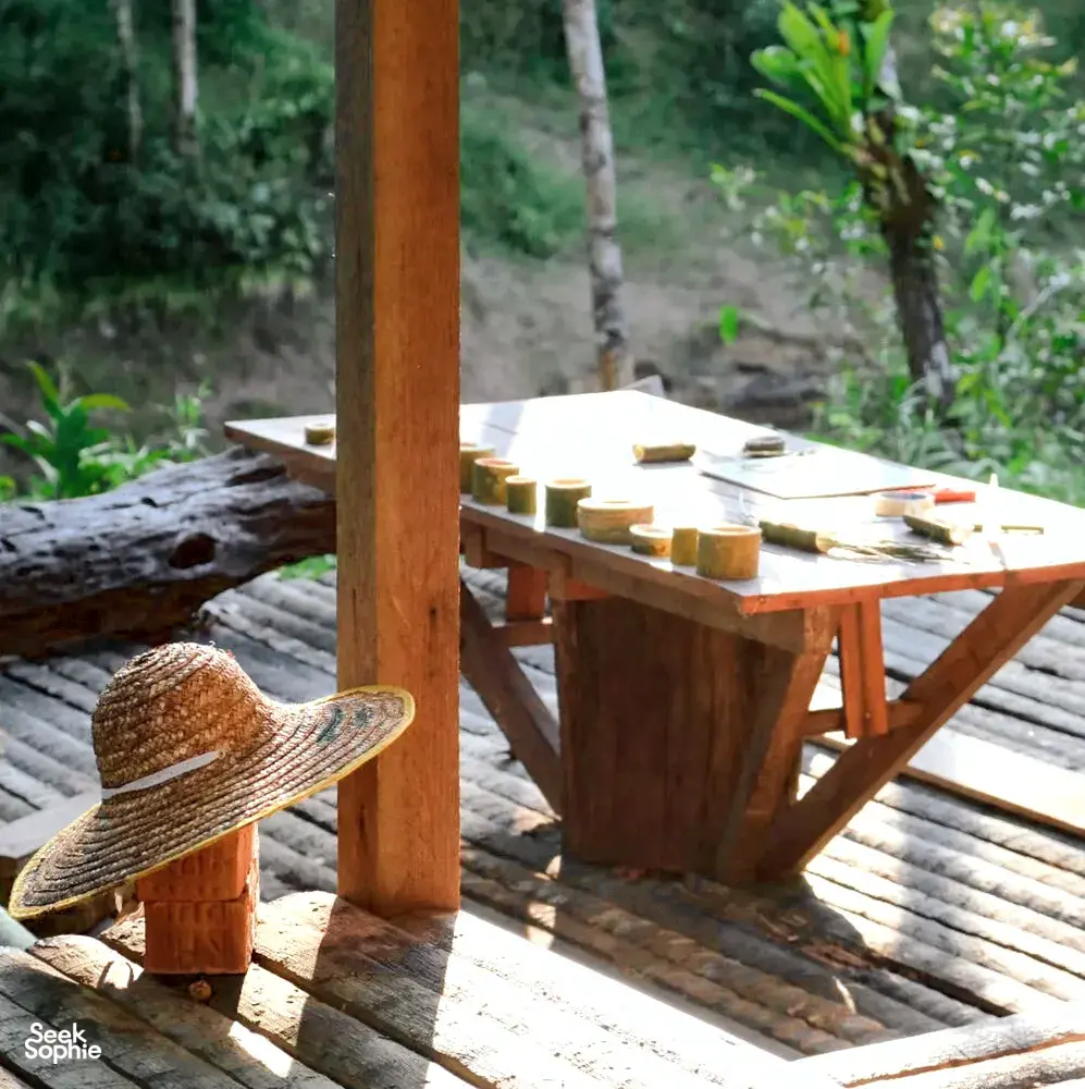 Rustic outdoor wooden dining table set with candles on Ngapuh Homesteadβs deck, jungle greenery behind, near Kuching