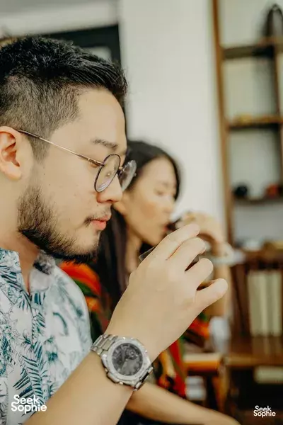 Man bringing a small cup close to his nose while guests watch during a rare agarwood tour tasting in Hanoi