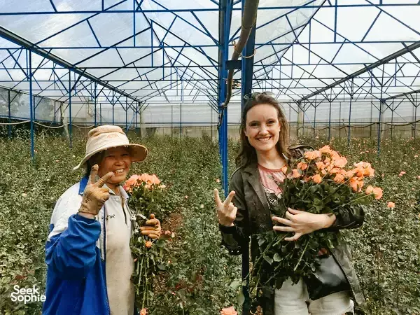 Smiling traveller and a child posing with fresh bouquets in a flower greenhouse near Da Lat on an Easy Rider stop