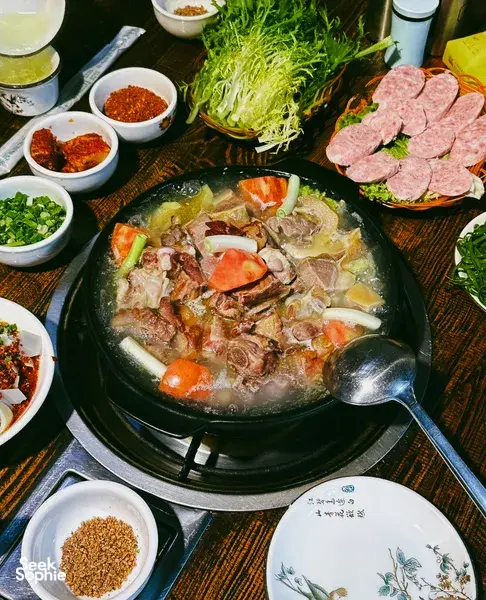 Hotpot tabletop in Lijiang with a bubbling central pot, sliced meats, shredded cabbage, and small bowls of chilli seasoning