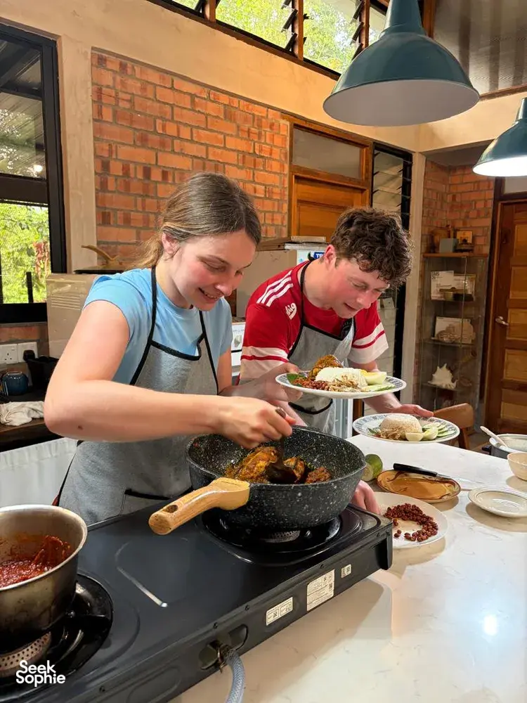 Guests tasting Malaysian comfort food in the Kebun Lidstari farmhouse kitchen in Langkawi, with a hot wok and spices on the stove