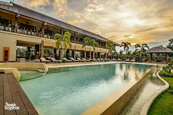Infinity-style resort swimming pool beside wooden decks, with palm-lined suites at The Island Lodge in the Mekong Delta