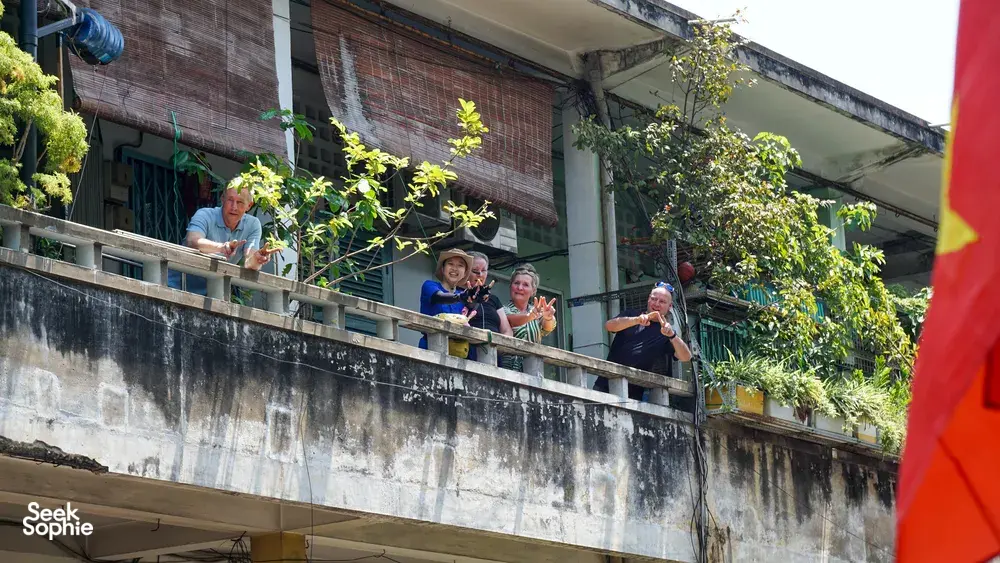 在菠萝蜜探险单车之旅中,客人们在胡志明市一条庭院街道上方的二楼阳台微笑挥手