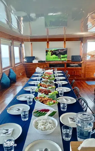 Set dining table aboard a wooden phinisi with shared plates, bowls and drinks during a 3D2N cruise to Komodo Island