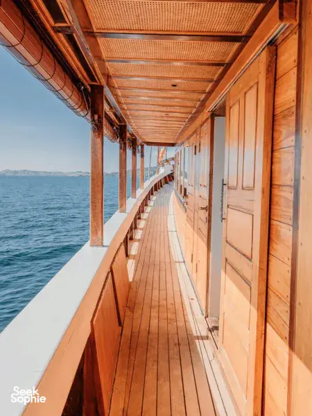 Covered wooden deck corridor on a deluxe phinisi with ocean views alongside during a 4D3N shared Komodo cruise, Komodo Island