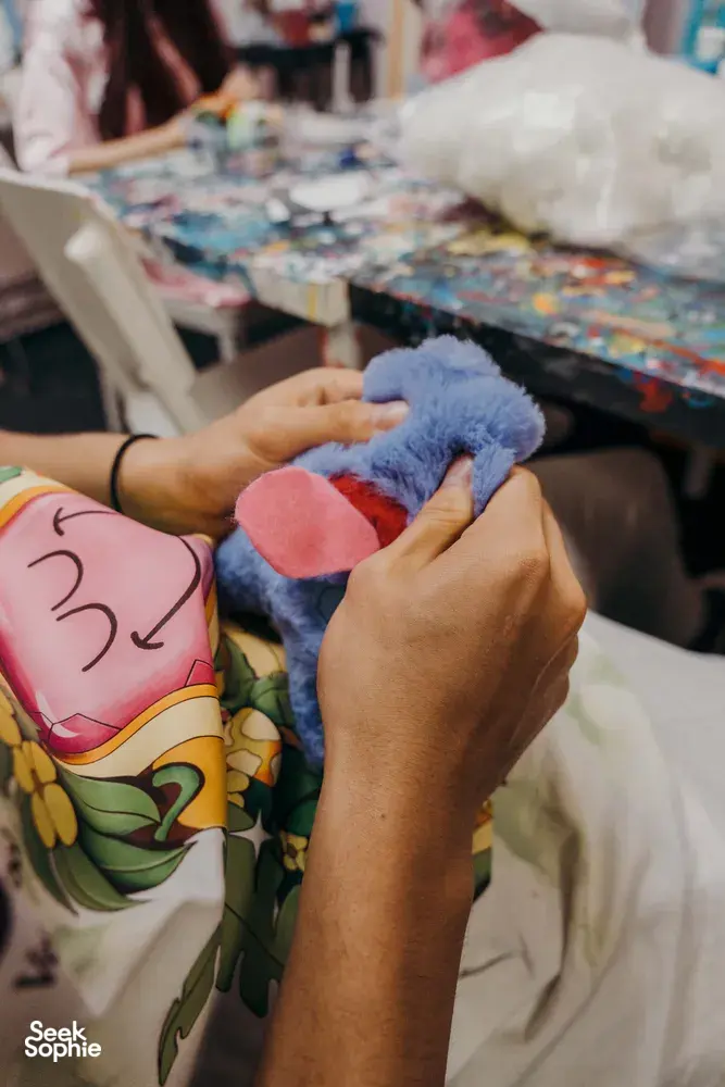 Close-up of hands stuffing a blue plush piece and attaching it to create an ugly-cute keychain in Singapore
