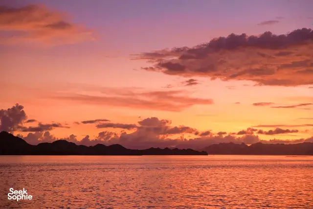 Warm golden sunset over the sea with distant island hills on the horizon, calm bay at dusk, Labuan Bajo