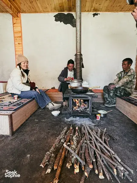 People warming by a wood-fired stove with pots in a guesthouse kitchen in Lijiang during the Yi & Naxi village trek