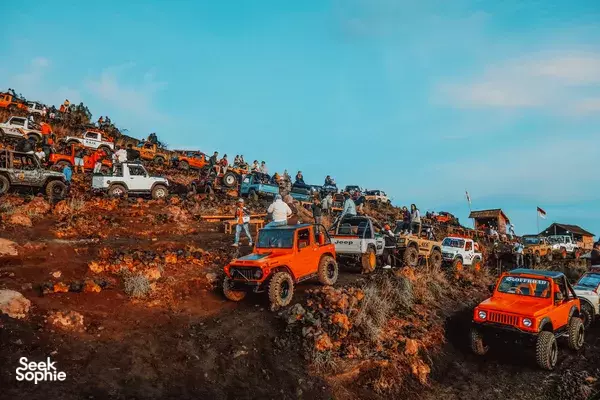 Orange 4x4 jeeps queue and climb a dusty ridge in an off-road convoy during the sunset near Bali’s Mt Batur