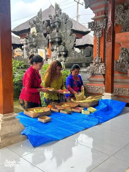 People arrange trays of colourful flower offerings on a blue cloth inside a Balinese temple courtyard during the visit in Bali