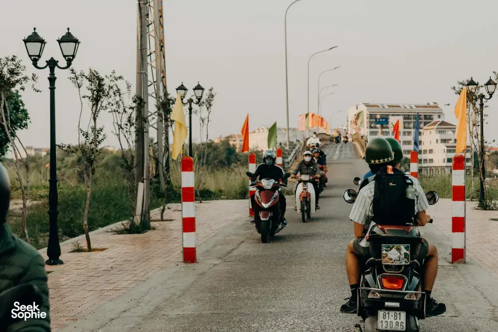 Pengendara berhelm mengikuti barisan skuter di jalan beraspal di Hoi An, bersiap berangkat untuk tur jalan belakang