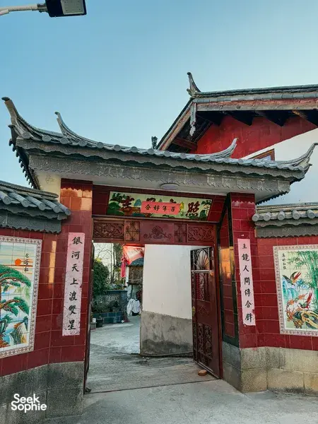 Traditional Naxi-style guesthouse entrance in Lijiang, Yunnan, with red door panels, ornate carvings and tiled roof eaves