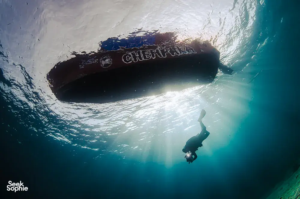 Diver silhouetted beneath a submerged shipwreck during a scuba dive, seen in Semporna’s clear ocean water