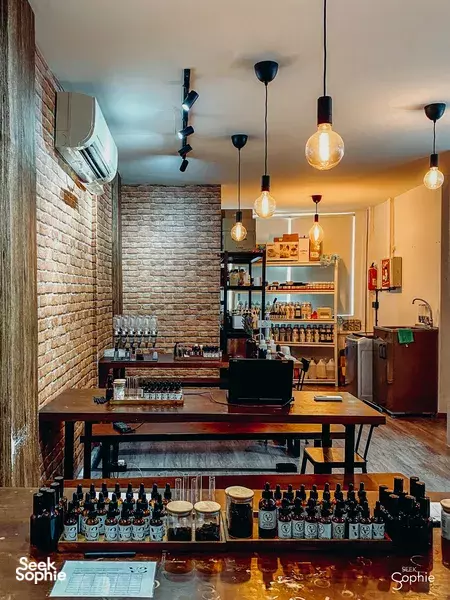 Essential-oil bottles and droppers on a bench beneath hanging lights in a brick-walled studio, for shower gel workshops in Singapore