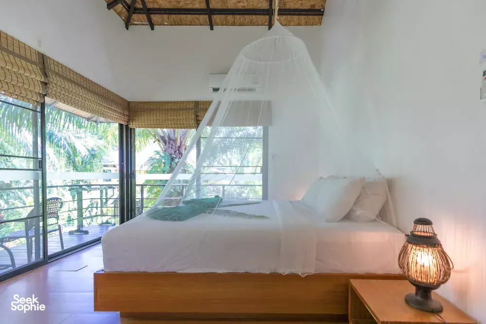 Canopy bed in a bright Anurak Lodge room at Khao Sok National Park, looking out to the jungle through sliding windows