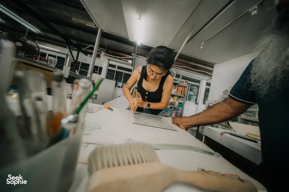 Glass centrepiece workshop in Singapore: a guest uses a tool to shape clear glass on a studio workbench, workshops in Singapore