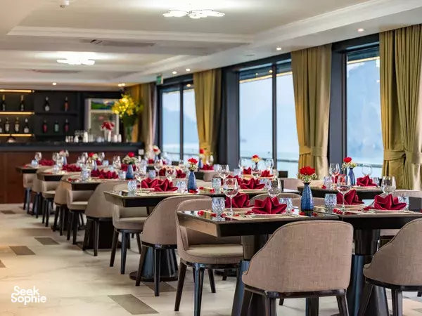 Doria Cruise on-board dining room set with red napkins and glassware, lined with large windows overlooking Halong Bay