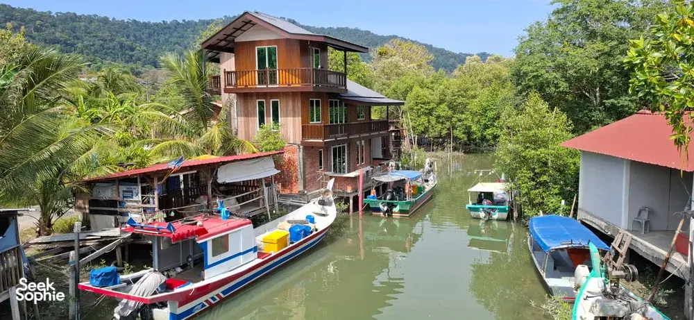 Boats moored along a Langkawi jetty beside stilted waterfront houses, part of a cycling tour through villages