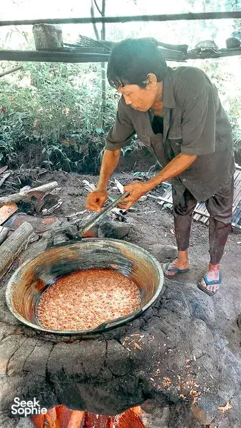 Former loggers' cooking in Lombok's forest: a local worker stirs ingredients in a large metal pot over open fire