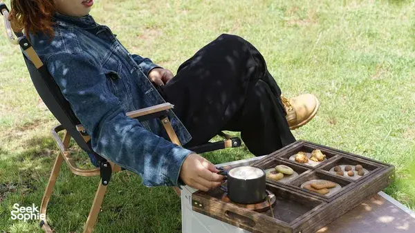 Outdoor coffee break at the Lijiang coffee estate: seated guest stirs snacks on a portable grill beside a tray of breads
