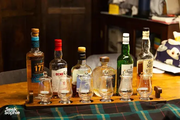 Row of whisky bottles and small tumbler glasses on a tray at a hidden home bar in Katong, Singapore, ready for small-batch tasting