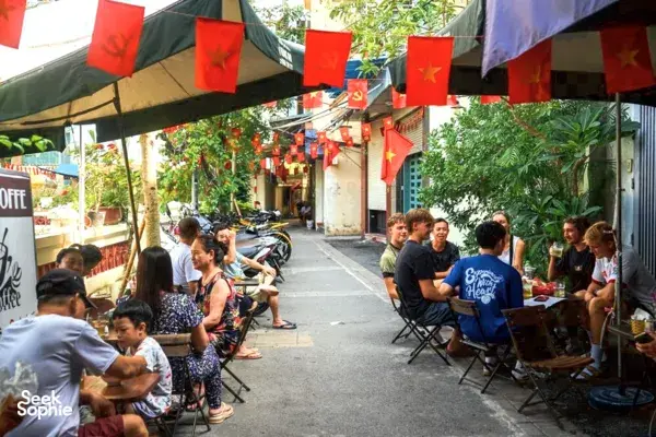 Cyclists take a break at a street café with Vietnamese flags in Hanoi during Jackfruit Adventure’s Hidden Wartime alley cycle