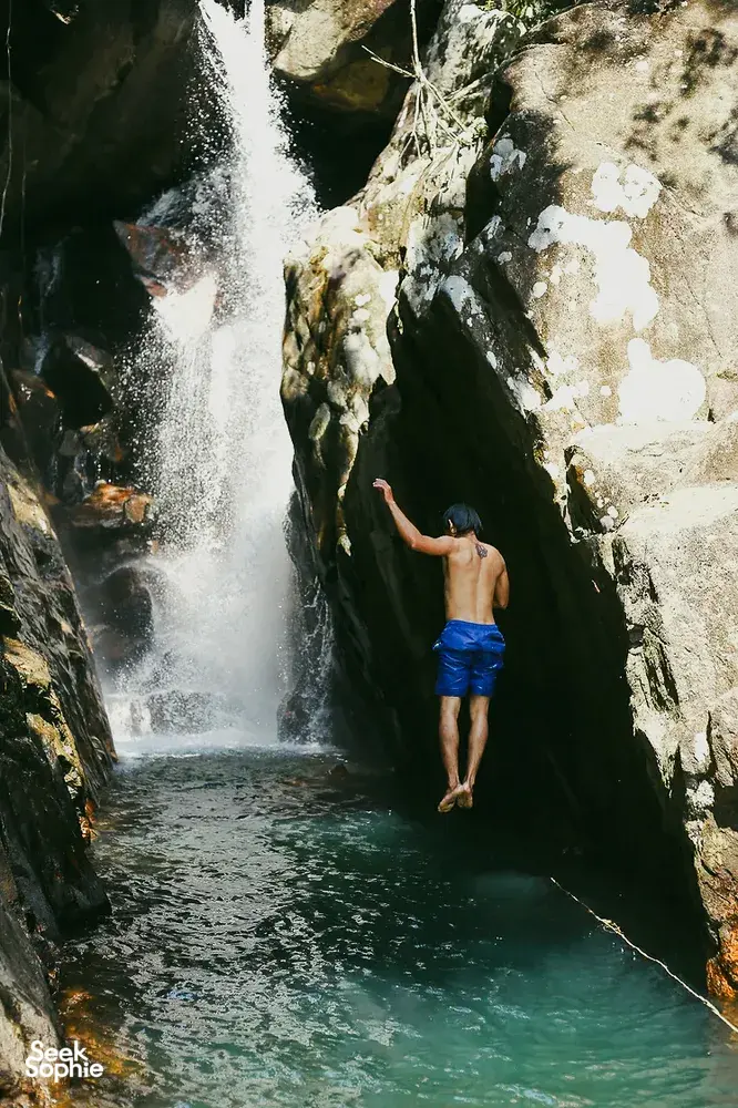 Nguyen Tours Hoi An secret waterfall stop on a motorbike adventure, a swimmer jumping into a turquoise pool by the falls