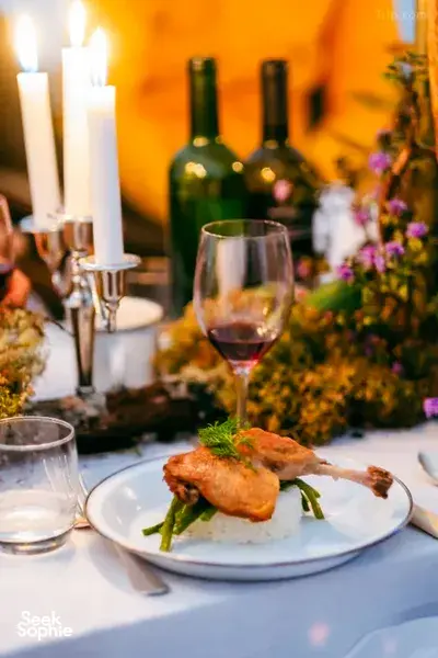 Candlelit 3-course dinner plate with sliced grilled chicken and herbs, with wine glasses on a table during Ferme Liotard’s trek