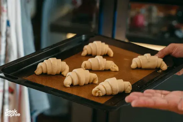 Tangan menyusun doh croissant berbentuk bulan sabit di atas dulang pembakar untuk bengkel memasak di rumah oleh French Cooking Lab di Singapura
