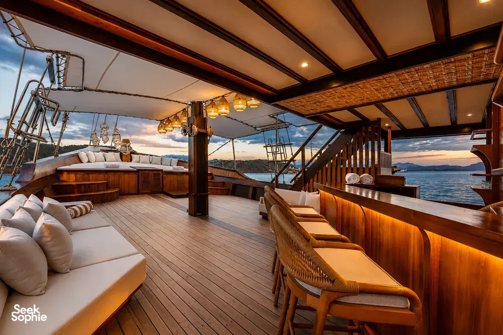 Sunset lounge deck of a Travass Life phinisi with cushioned benches, wooden railings and open sea views, on Komodo Island